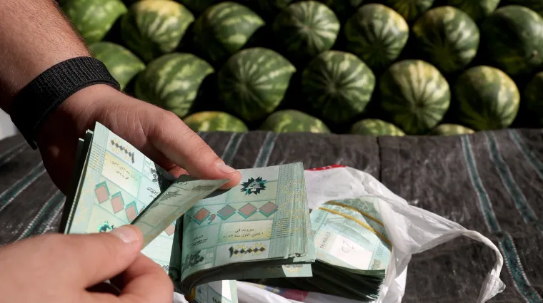 A watermelon producer counts cash bills at a fruit and vegetables outside Beirut