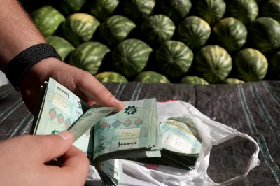 A watermelon producer counts cash bills at a fruit and vegetables outside Beirut