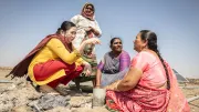 Woman in India sit near a solar panel in a desert. 