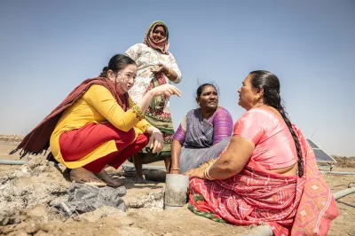 Woman in India sit near a solar panel in a desert. 