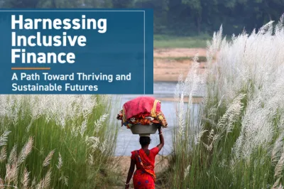 a woman in a red sari carries a basket of laundry on her head walking through a field towards the water